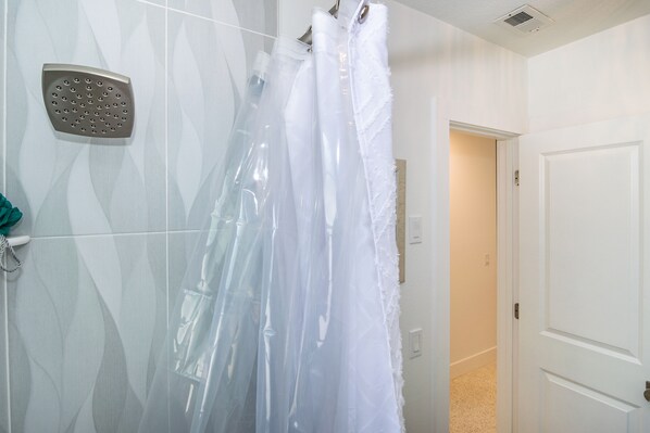 A shower with a transparent curtain, a handheld showerhead, and a white door in the background. - Made in Shade B · Beach Across St · Pets OK (Holmes Beach)