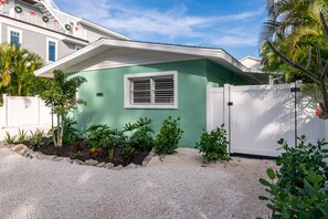 Une petite maison à un étage, à l’extérieur vert, avec des volets blancs et une clôture blanche.