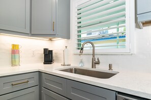 Eine moderne Küche mit grauen Schränken, einer Edelstahlspüle und einem Fenster mit Jalousien.