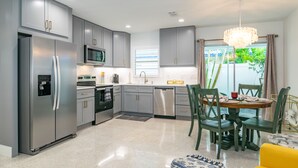 A modern kitchen with grey cabinets, stainless steel appliances, and a dining area with a yellow sofa and green chairs. - Made In The Shade A &B | Multiple Units (Holmes Beach)