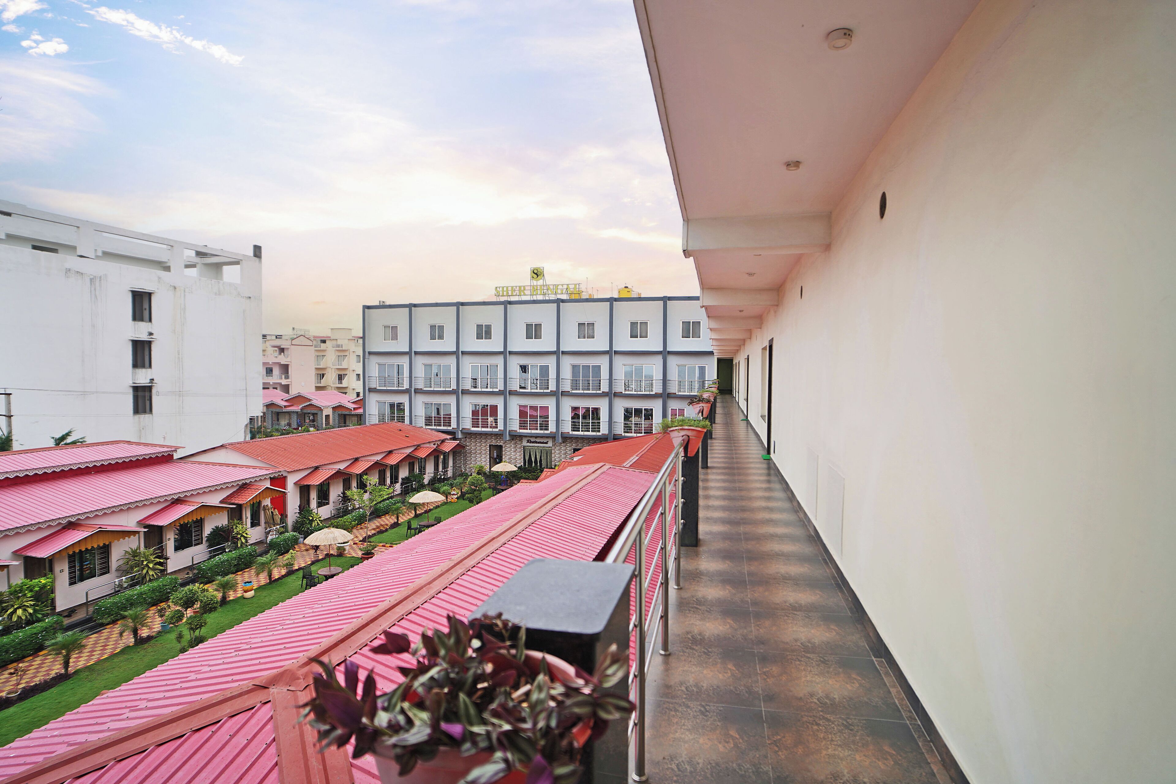 A corridor with a balcony, a row of buildings with red roofs, and a clear sky.