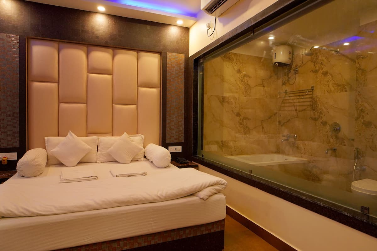 A hotel room with a large bed, a glass-enclosed shower, and a marble wall.