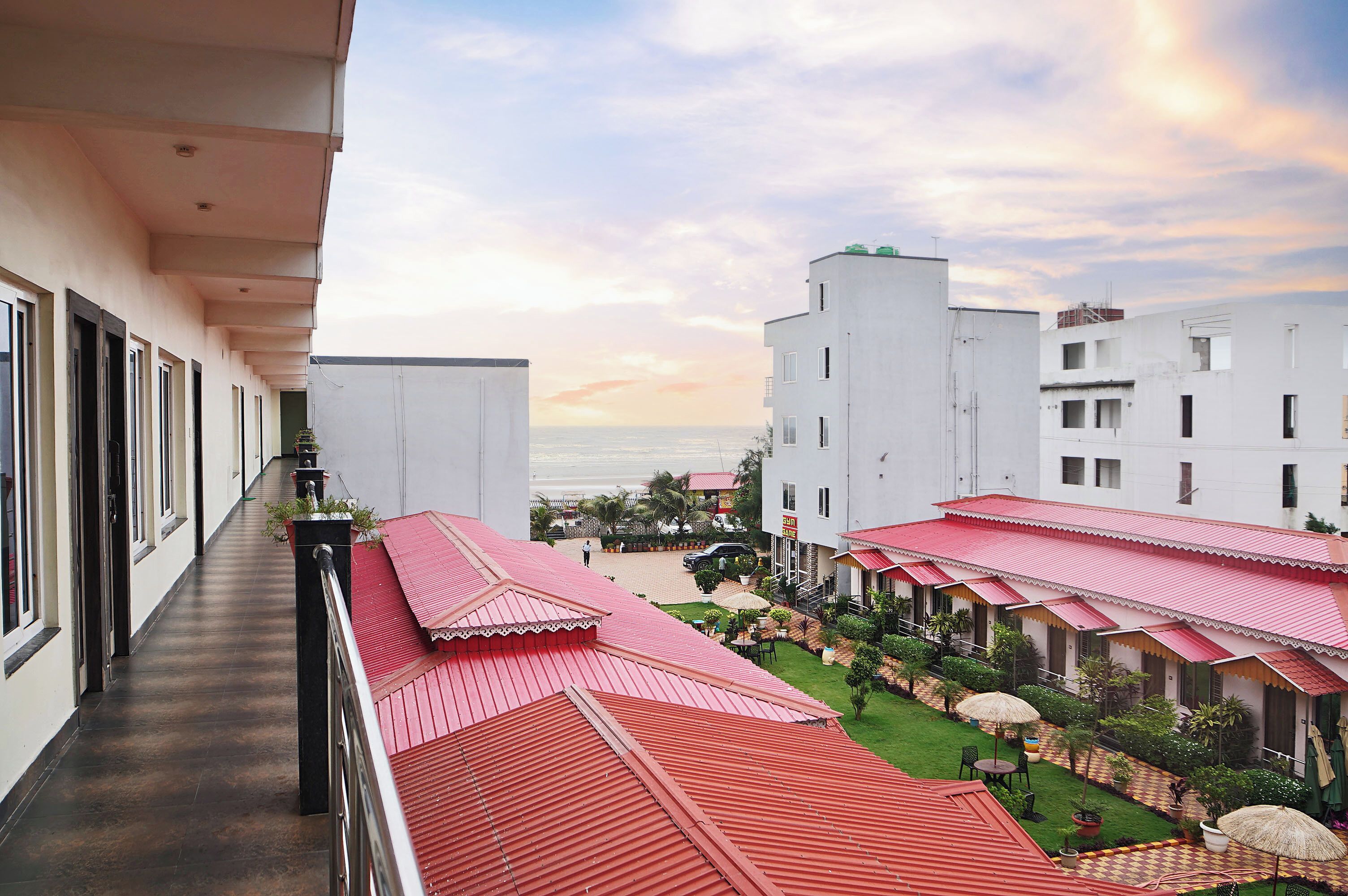 Un hotel con balcón que da a un patio con edificios de tejados rojos, vista al mar y cielo despejado.