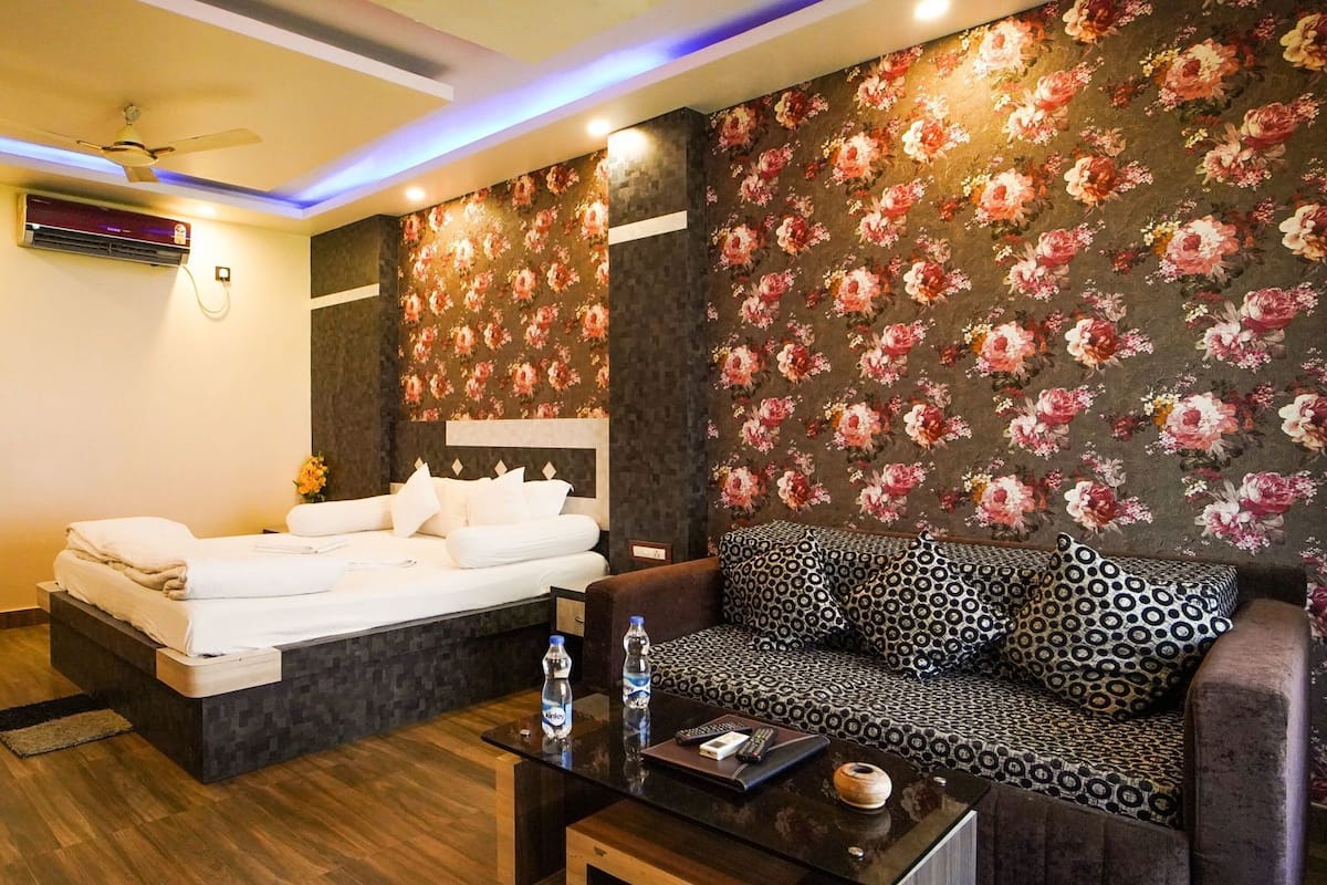 A hotel room with a bed, a sofa, a coffee table, and a wall with floral wallpaper.