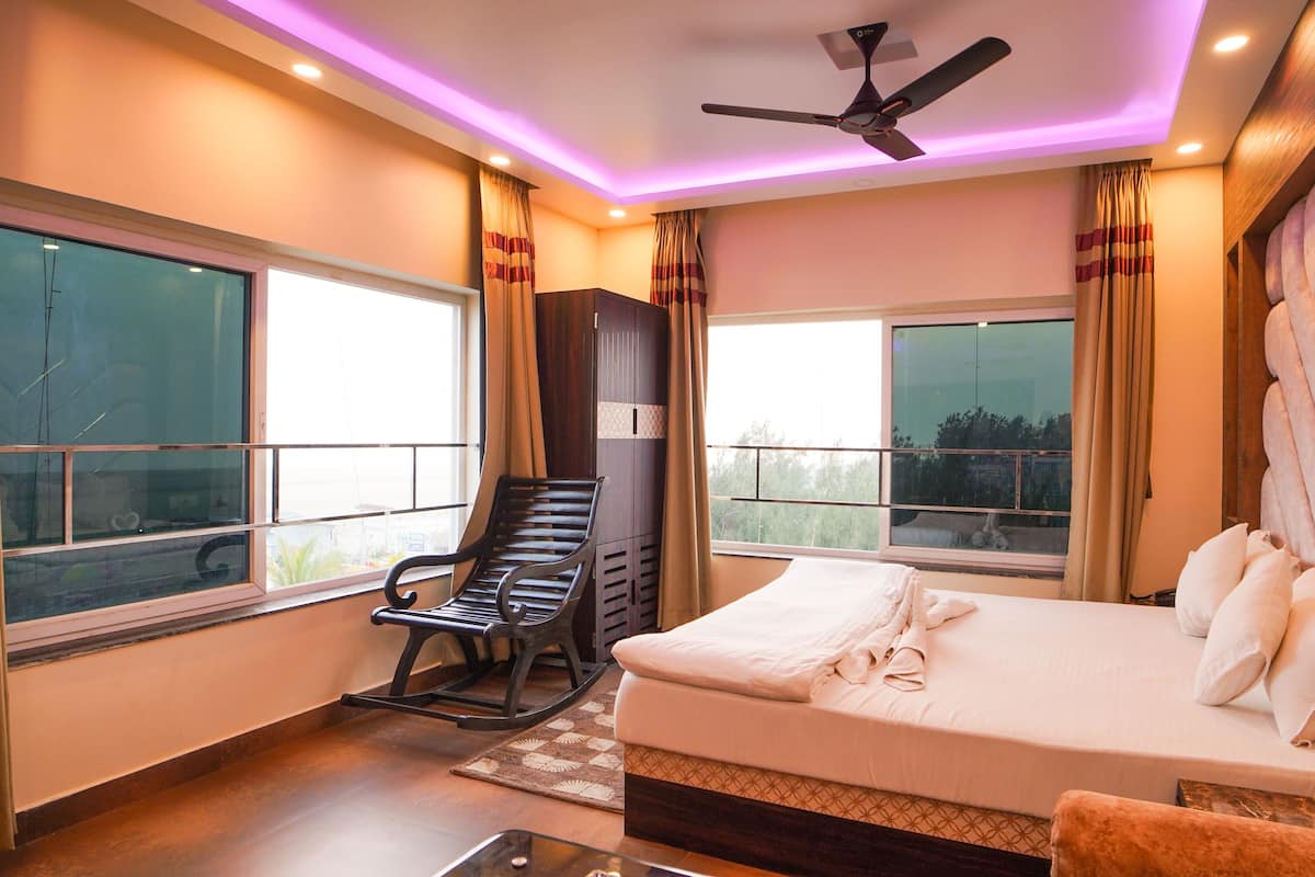 A bedroom with a bed, a reclining chair, a ceiling fan, and large windows.