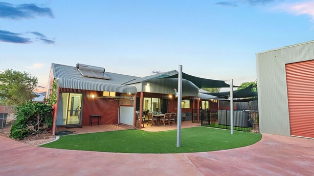A modern house with a covered patio, a fenced backyard, and a red garage.
