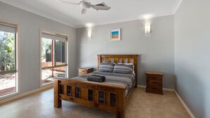 A bedroom with a wooden bed, a nightstand, a bedside table, a ceiling fan, and a window with a view of greenery.