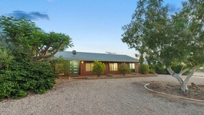 A single-story building with a gravel driveway, surrounded by greenery and trees.