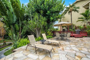 Une terrasse extérieure avec un sol en pierre, des fauteuils et une petite table.