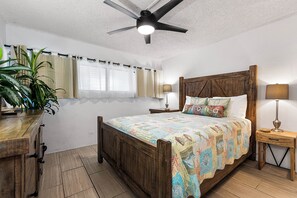 Une chambre à coucher avec un lit en bois, un ventilateur de plafond, une table de chevet, une lampe et une plante en pot.