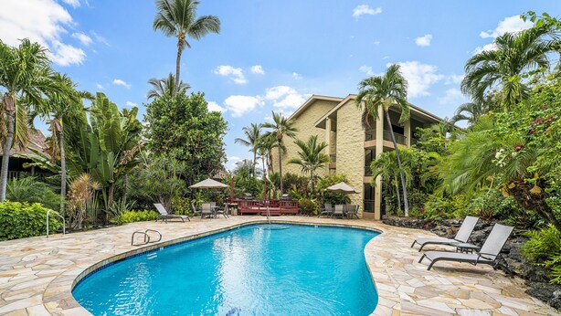 A swimming pool with stone tiles, surrounded by palm trees and lounge chairs. - Kalani Kai#109 1st Floor, Remodeled Unit in Heart of Kona Town! Best location (Kailua Kona)