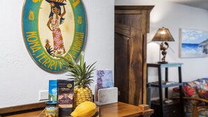 A wooden table with a pineapple, a bottle of rum, a laptop, and a framed sign reading "Kona Terri". - Kalani Kai#109 1st Floor, Remodeled Unit in Heart of Kona Town! Best location (Kailua Kona)