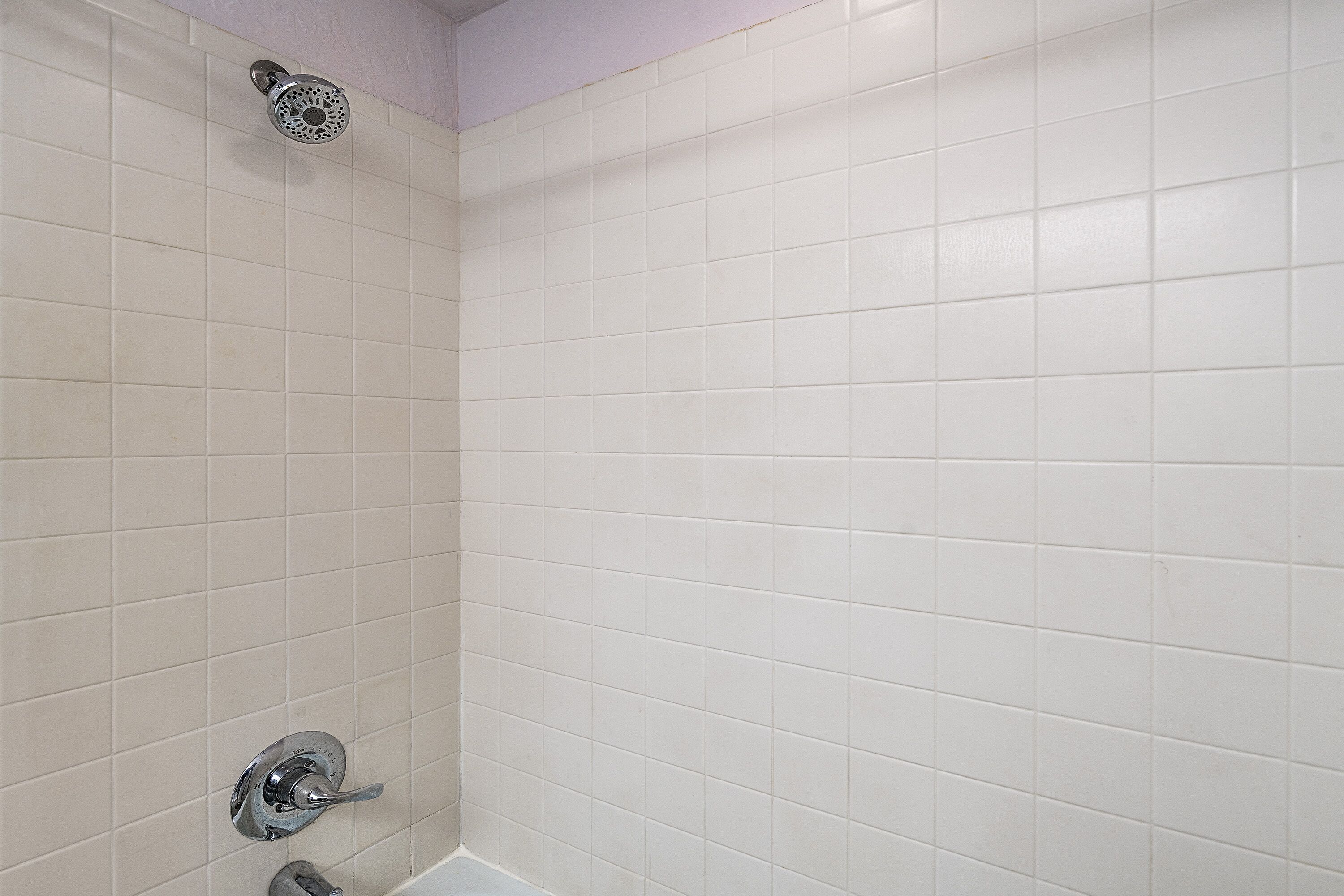 Une salle de bain avec des murs recouverts de carreaux blancs, une pomme de douche et un robinet.