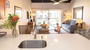A kitchen with a large island, a dining area with wicker furniture, a sofa, and a ceiling fan.