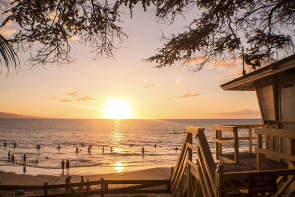 A beach scene with a sunset, wooden beach chairs, and a lifeguard tower.