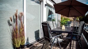 Une terrasse extérieure avec une table et des chaises, un grand parasol et des plantes décoratives.