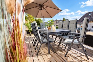An outdoor patio with a table and chairs, a large umbrella, and a view of houses in the background.