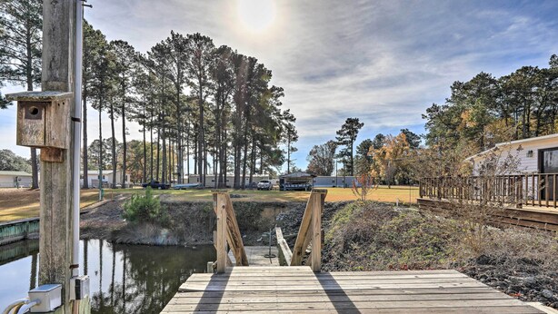 A wooden bridge leading to a dock over a calm body of water, surrounded by tall trees and a clear sky. - Pet-Friendly Cabin w/ Dock: Fish & Explore! (Oriental)