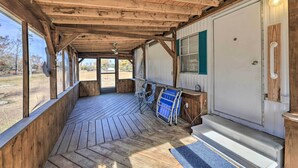 A covered porch with wooden beams, a folding chair, a blue folding table, and a white door with a window. - Pet-Friendly Cabin w/ Dock: Fish & Explore! (Oriental)
