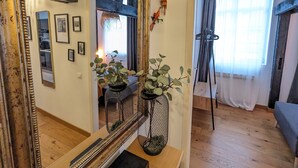 Ein Zimmer mit einem großen Spiegel, Holzbalken, einer Pflanze, einer Hängelampe und einem Fenster mit Vorhängen.