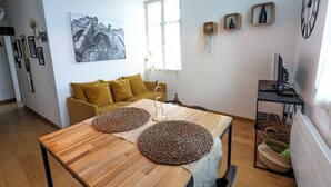 Ein modernes Wohnzimmer mit einem Holzesstisch, einem senffarbenen Sofa und einem großen Fenster.