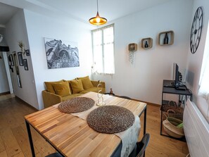 A modern living room with a wooden dining table, a mustard-colored sofa, and a large window.