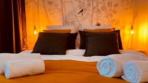 Ein ordentlich bezogenes Bett mit aufgerollten Handtüchern, zwei schwarzen Kissen und einem weißen Kissen.