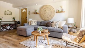 Una sala moderna con un sofá seccional gris, una pieza decorativa circular tejida en la pared y una mesa de centro de madera.