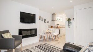 Un salon moderne doté d’une cheminée, d’un téléviseur à écran plat, d’un canapé et d’un coin repas avec une petite table et des chaises.