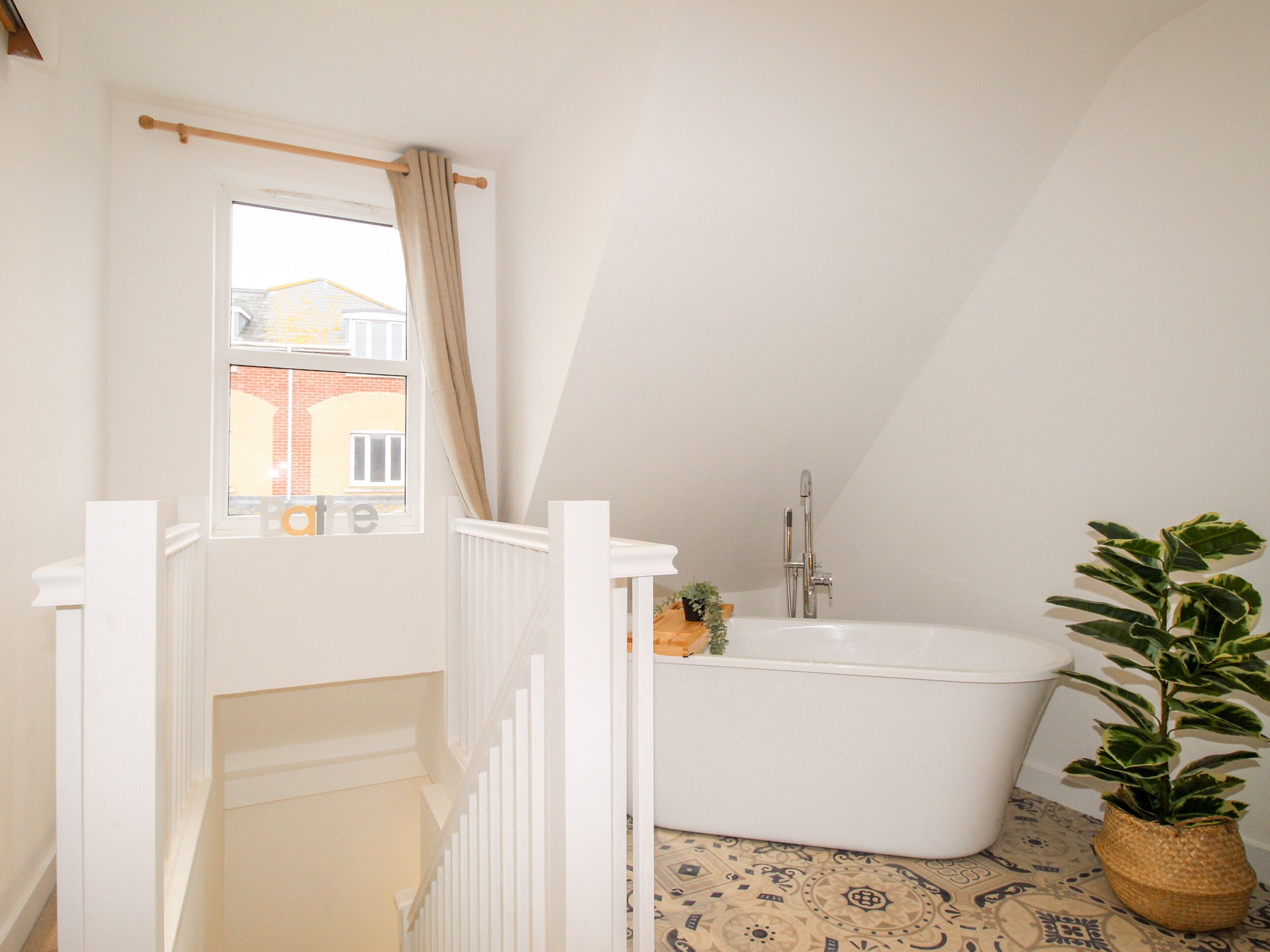 A bathroom with a freestanding bathtub, a window with a view of buildings, and a potted plant.