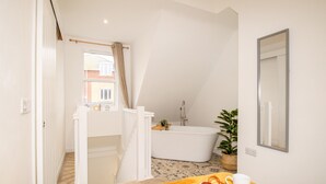 Une salle de bain avec une baignoire, une douche et une fenêtre avec des rideaux. On y trouve une plante sur le sol et un porte-serviettes.