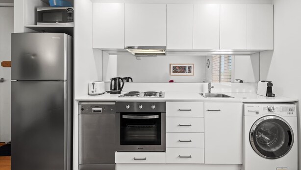 A compact kitchen with a refrigerator, oven, microwave, and washing machine.