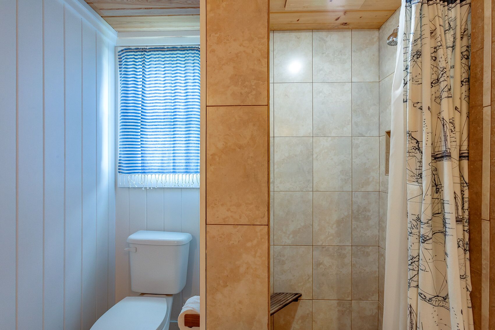 A bathroom with a toilet, a window with striped curtains, and a shower area with patterned curtains.
