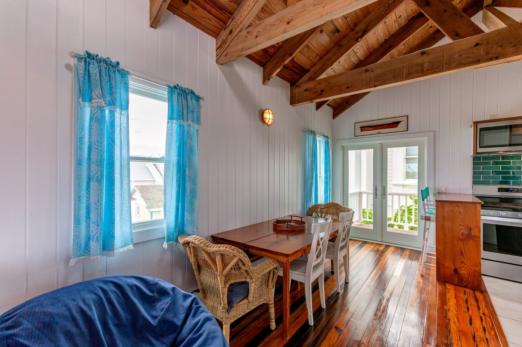 A cozy room with a wooden dining table, wicker chairs, a blue sofa, and a kitchen area with a stove.