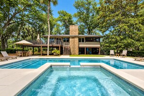 A two-story house with a swimming pool, outdoor furniture, and a covered patio area.