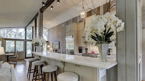 Une cuisine moderne dotée d’un grand îlot central, de tabourets de bar et de deux grands arrangements floraux.