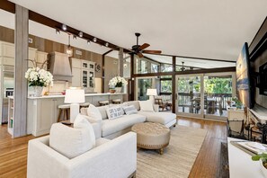 A modern kitchen with a large island, a dining area with a view, and a living room with a sofa and ottoman.