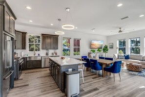 A modern kitchen with dark cabinets, a central island, and a dining area with blue chairs.