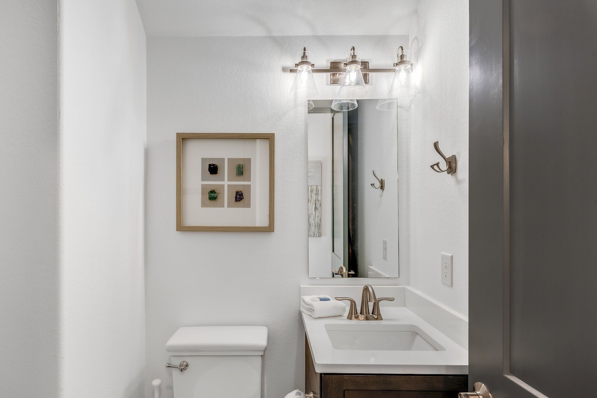 Un baño con inodoro blanco, lavamanos con espejo encima y un cuadro en la pared.