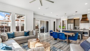 A spacious living area with a sofa, coffee table, and dining table with chairs. There is a kitchen area with modern appliances and a ceiling fan. - Luxe 4BR 30A Retreat w/ Private Pool & Golf Cart (Santa Rosa Beach)