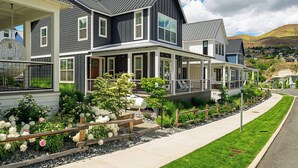 A two-story house with a covered porch, a landscaped garden with flowers and shrubs, and a hilly landscape in the background. - Welcome to Skylake Cottage at The Lookout at Lake Chelan (Chelan)
