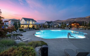 Una piscina con lettini, un edificio con numerose finestre e montagne sullo sfondo.