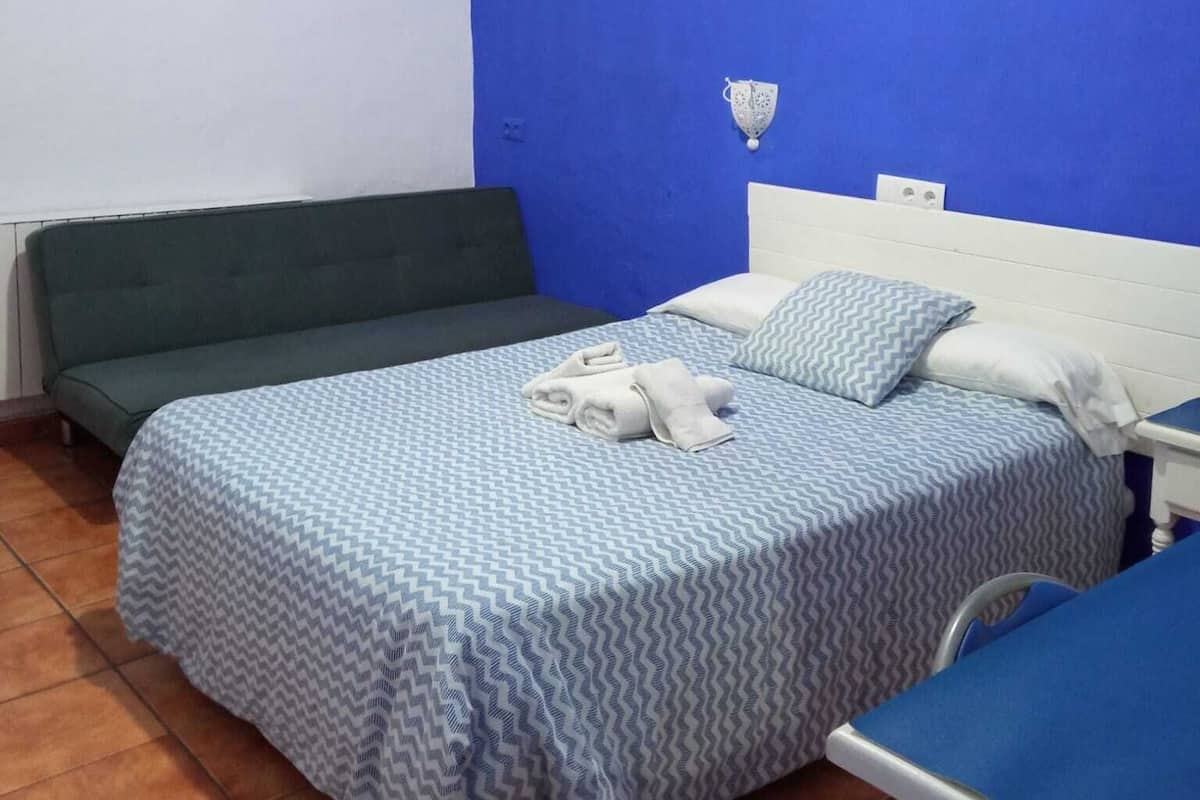 Ein Zimmer mit einem Bett, einem grünen Sofa, einer blauen Wand und einem weißen Nachttisch.