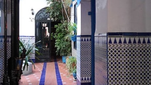 Um corredor com paredes e chão azulejados em azul e branco, e uma porta no final.