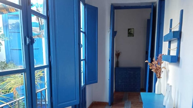Um corredor com portas e janelas azuis, chão de azulejos e um armário azul com um vaso.