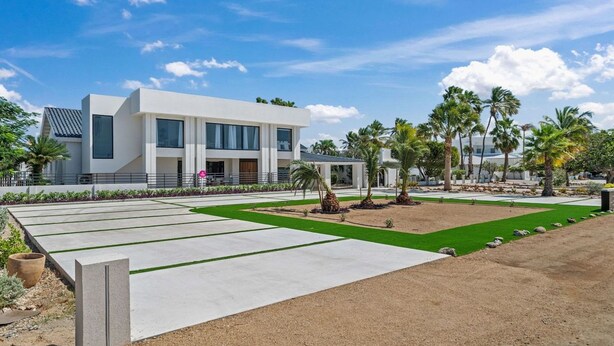 A modern building with a flat roof, large windows, and a landscaped garden with palm trees and a lawn. - Ocean Front! 8BR Villa with Pool near Malmok Beach (Malmok)