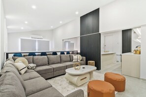 A modern living room with a sectional sofa, a coffee table, and ottomans. There is a kitchen area with a countertop and cabinets. - Ocean Front! 8BR Villa with Pool near Malmok Beach (Malmok)