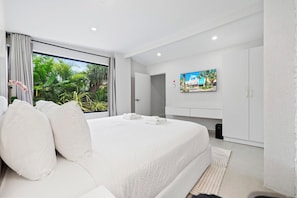 A modern hotel room with a large bed, a television mounted on the wall, and a view of greenery outside. - Ocean Front! 8BR Villa with Pool near Malmok Beach (Malmok)