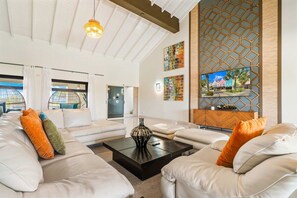 A modern living room with a sofa set, a coffee table, and a television mounted on a wooden panel. - Ocean Front! 8BR Villa with Pool near Malmok Beach (Malmok)