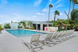 Ein Swimmingpool mit Liegestühlen, umgeben von Palmen und einem wolkenlosen Himmel.